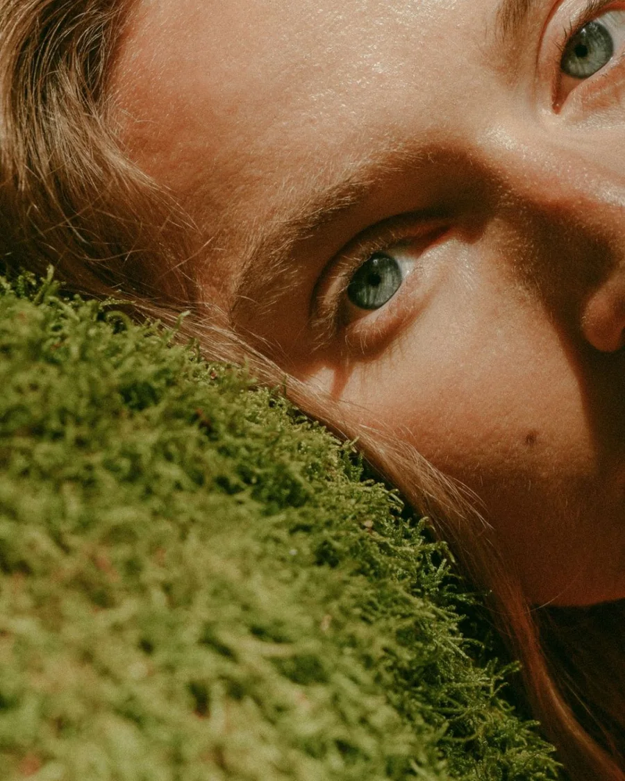 A woman's face resting against a mound of green moss