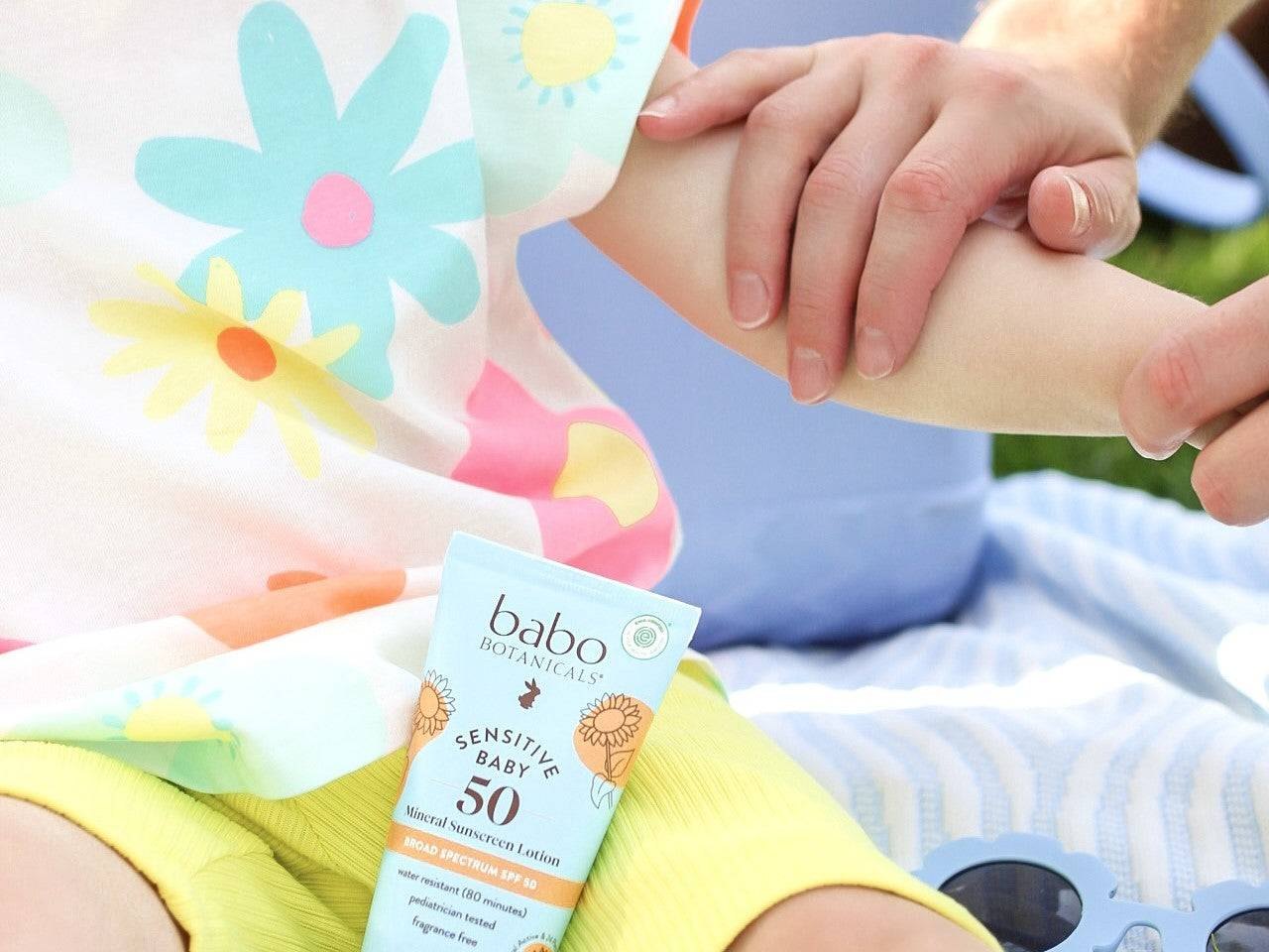 Adult applying Babo sunscreen to a childs arm outdoors.