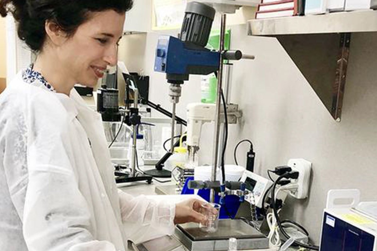 Woman in lab coat working with beaker at lab bench.
