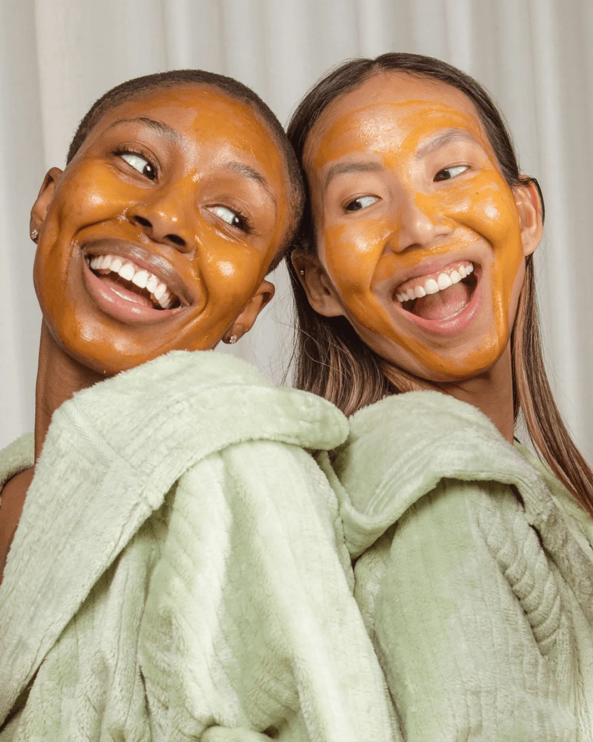 Two women wearing Hyper Fade and Glow mask smile.