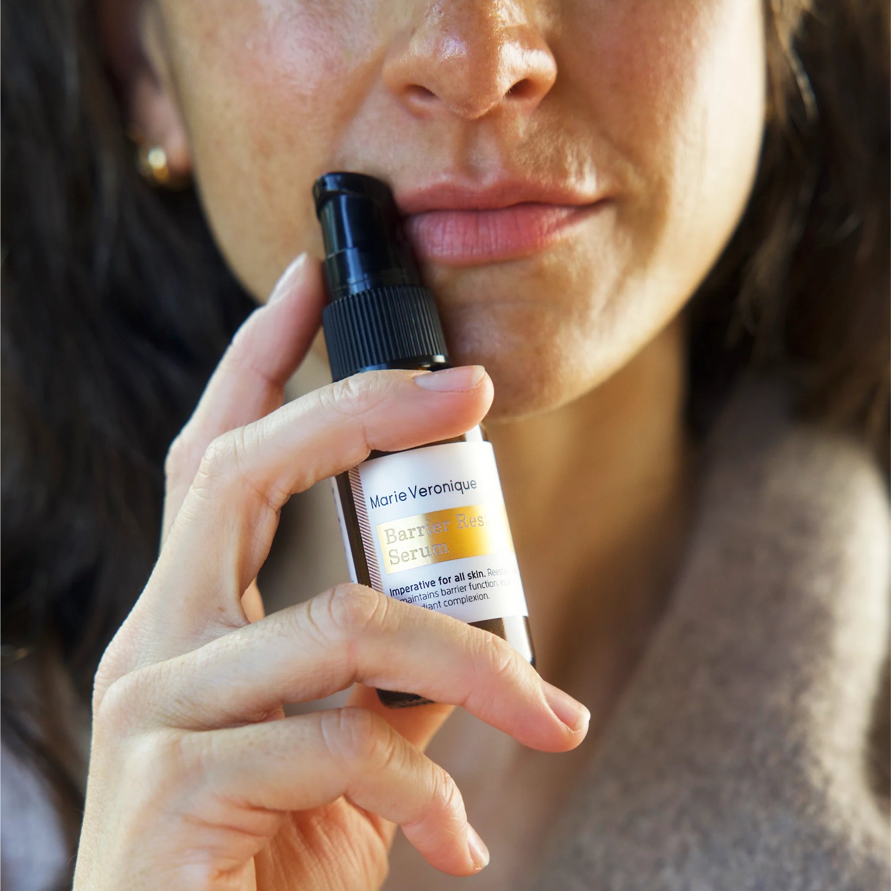 Woman holding Barrier Restore Serum bottle close to face.
