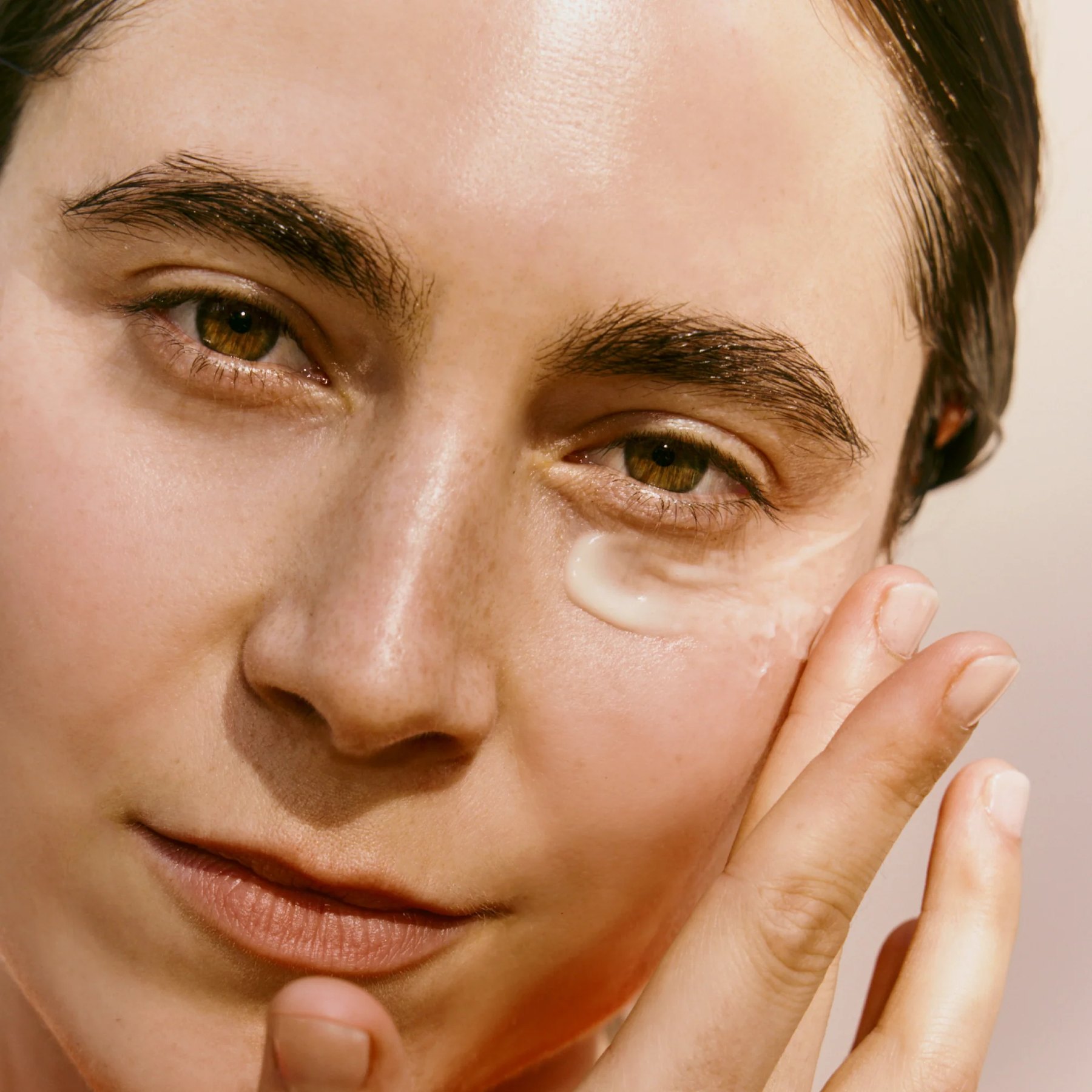 Woman applying cream to skin under her eye.
