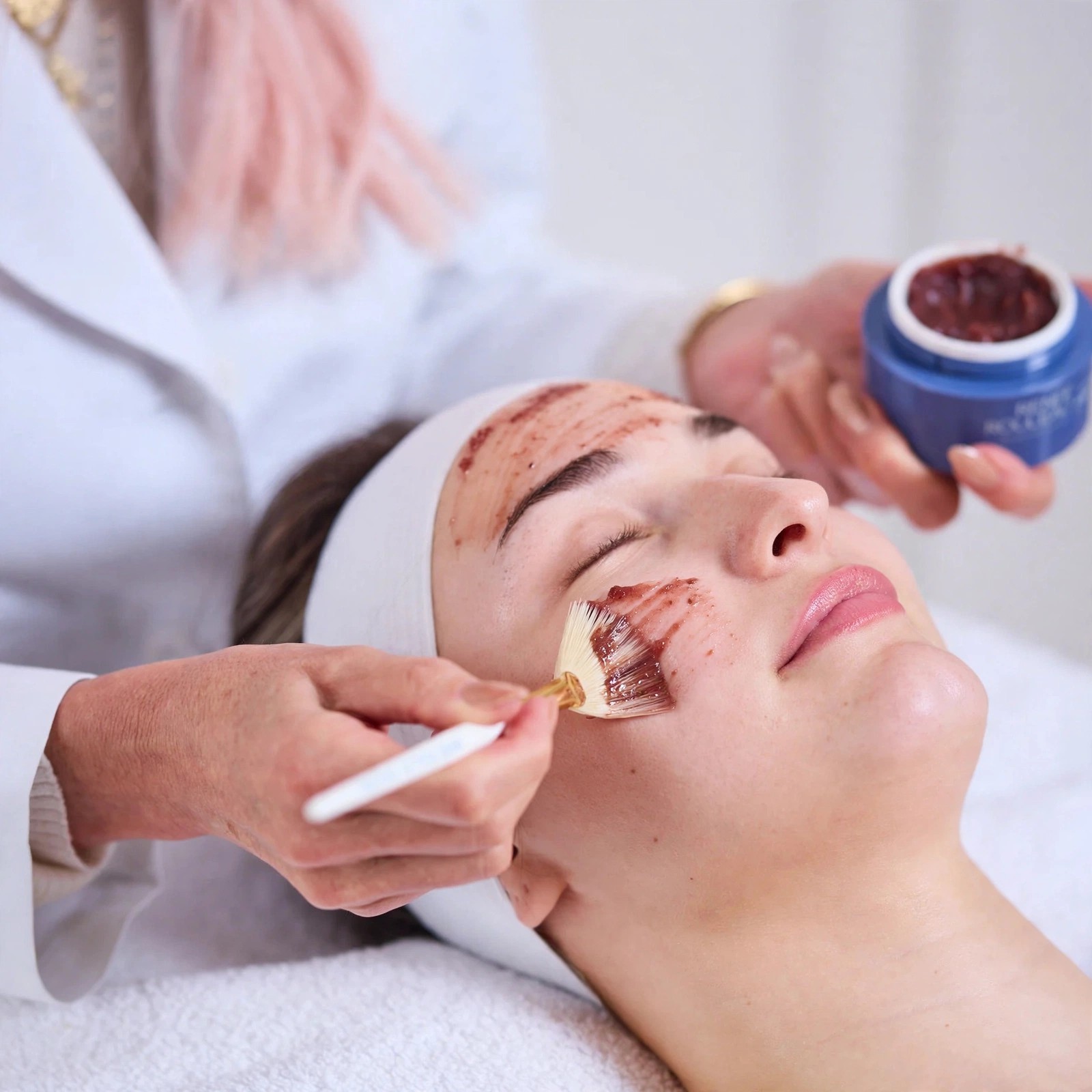 An esthetician applies berry peel to a clients face with brush.