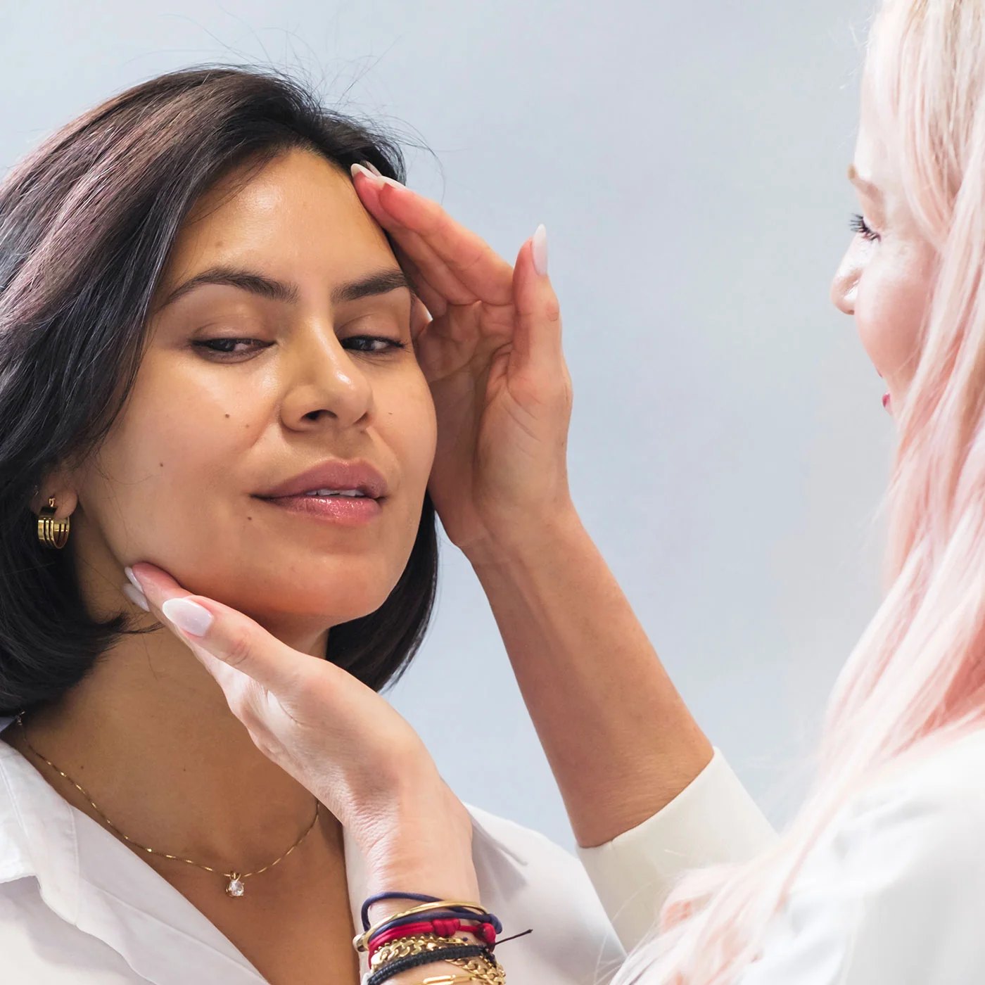 An esthetician with pink hair examines a clients facial skin.