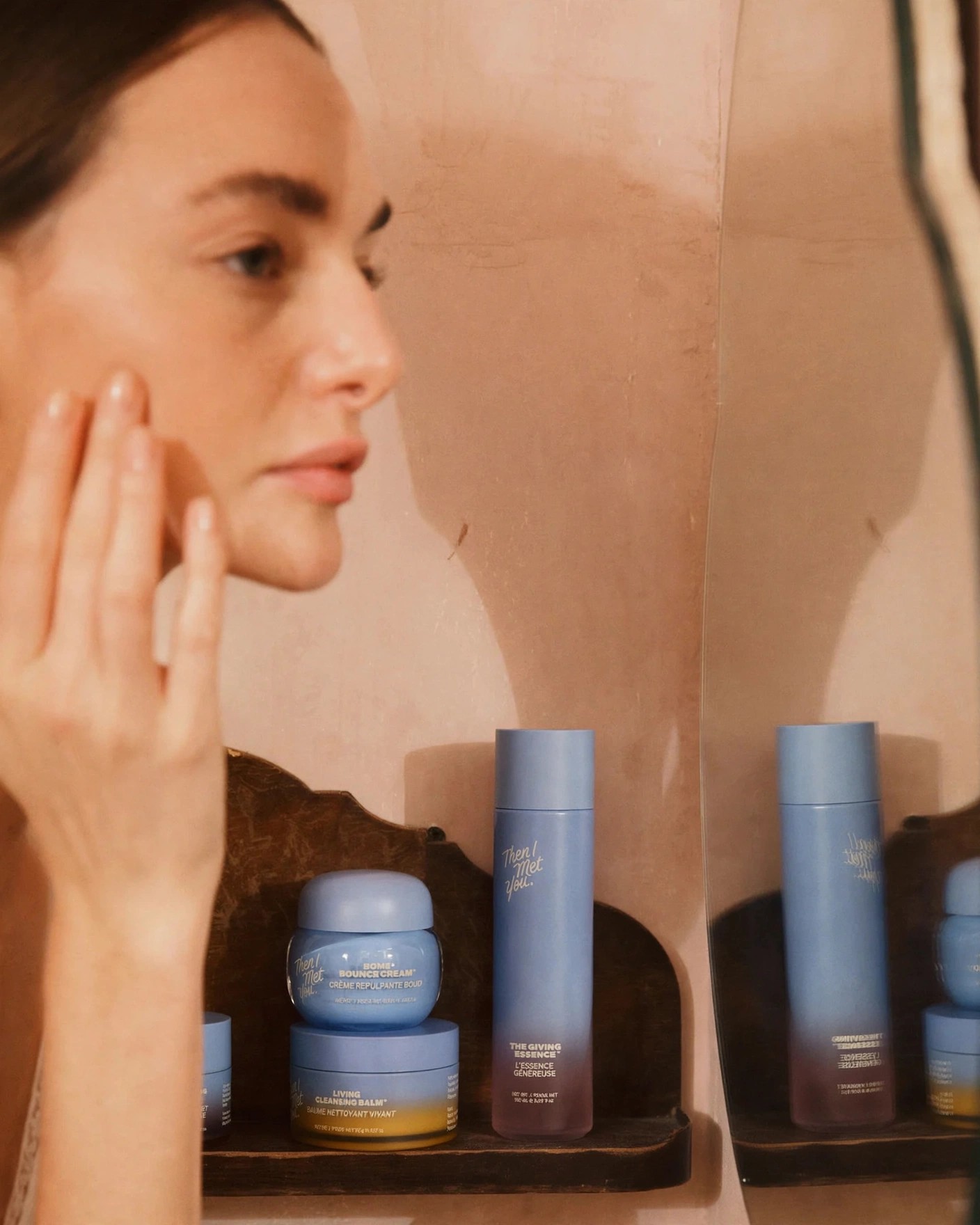 Woman touches her face beside shelf of blue skincare products.