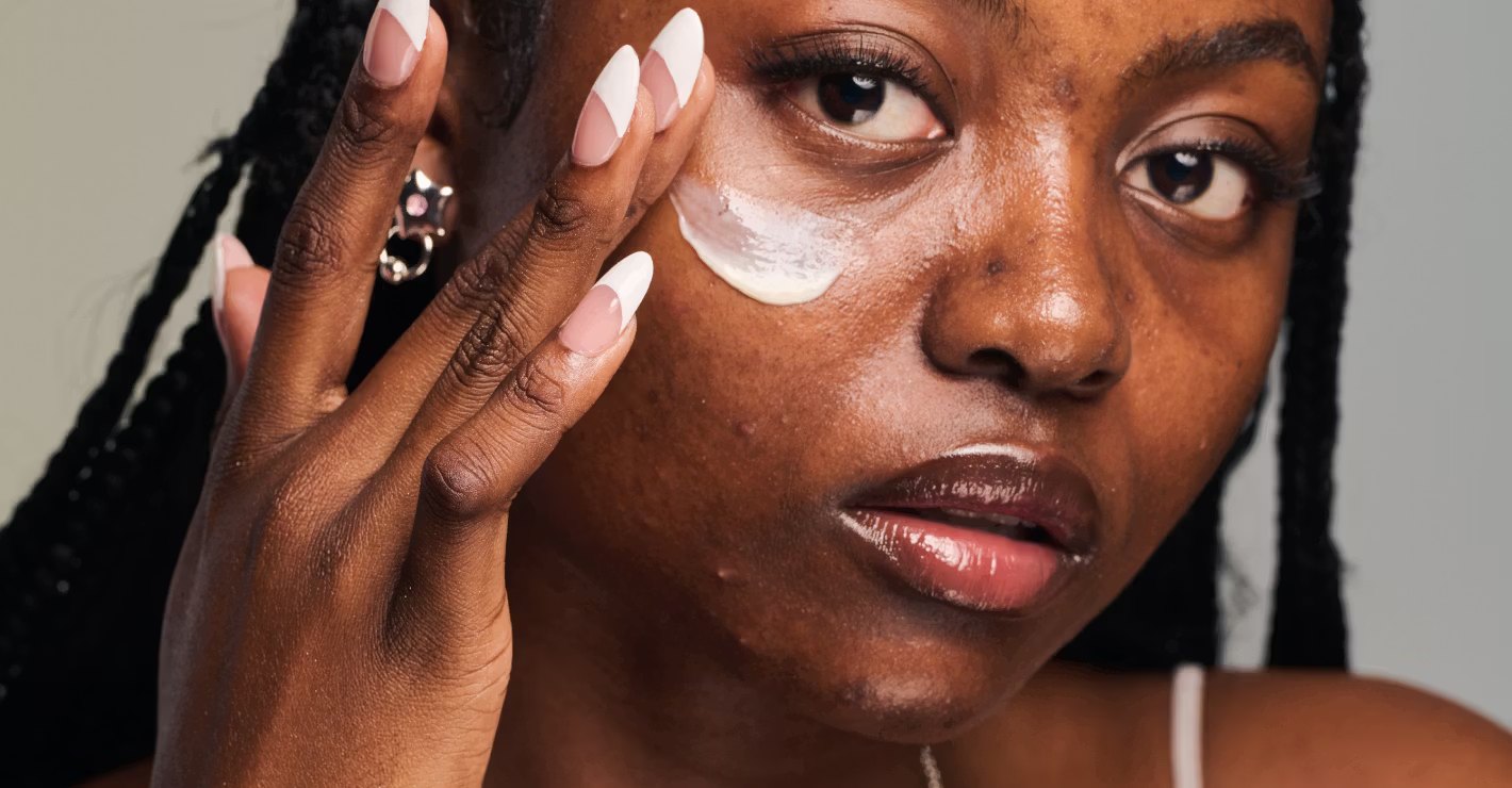A woman with braided hair applies cream to her cheek.