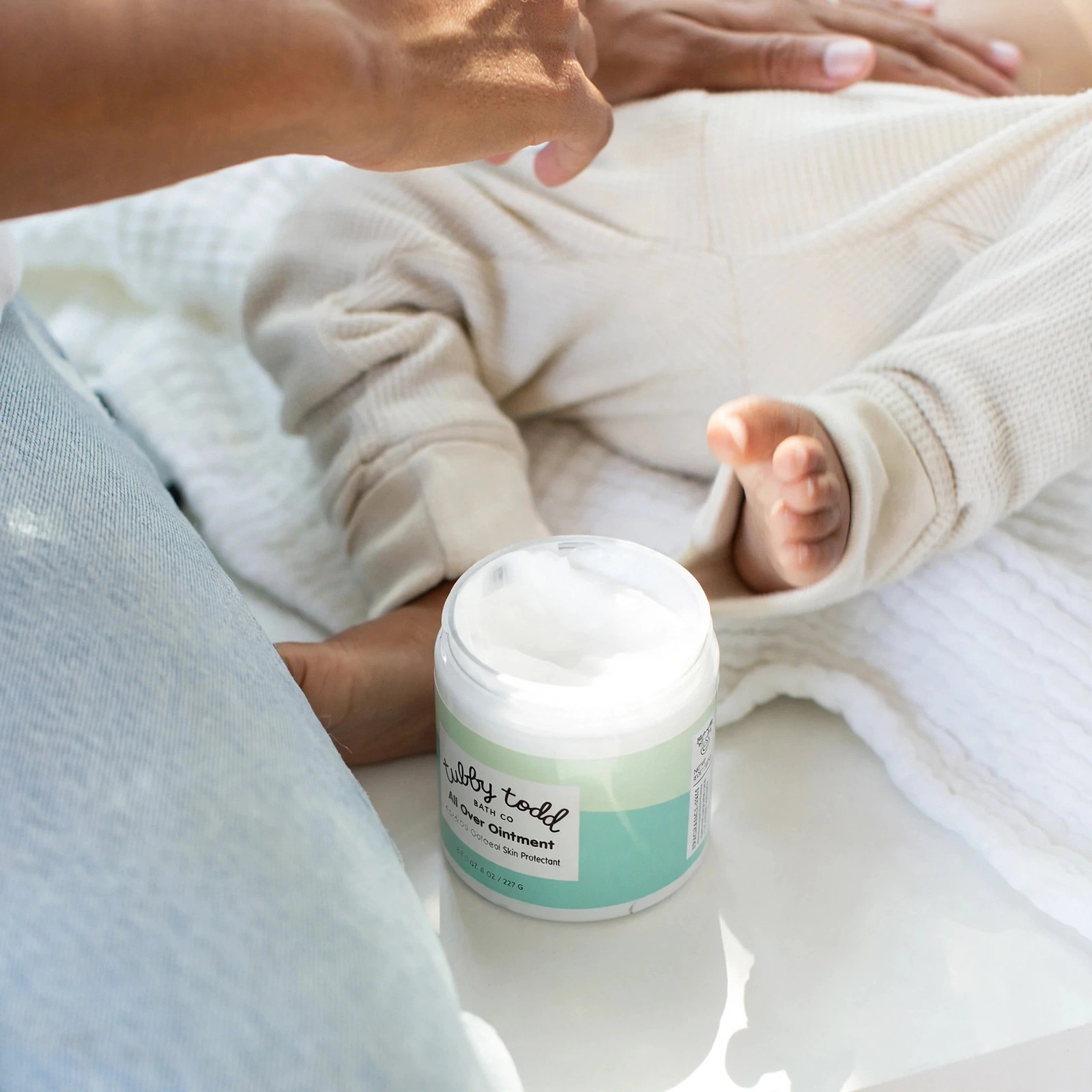 Open All Over Ointment jar beside a baby being dressed.