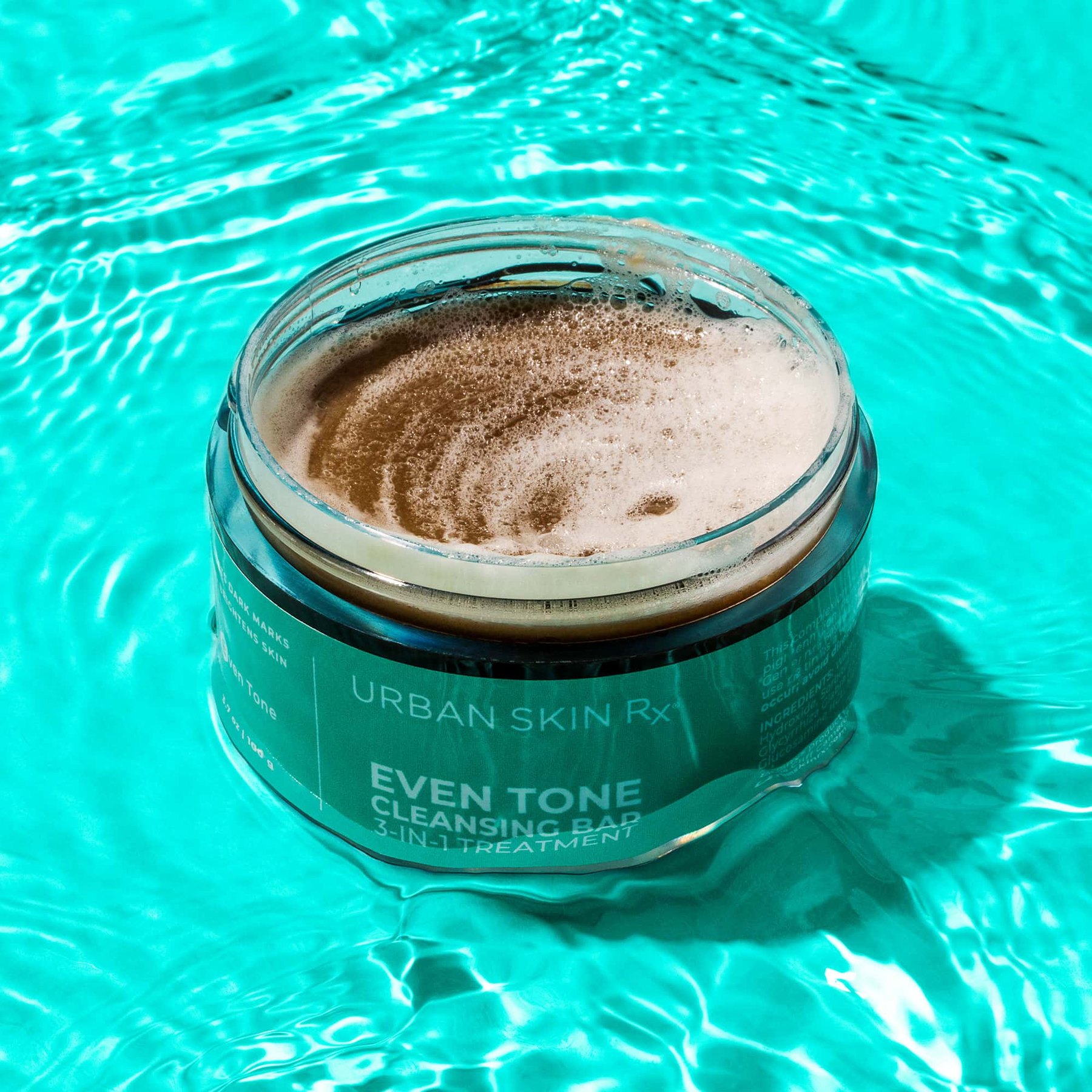 Open jar of Even Tone Cleansing Bar with lather in water.